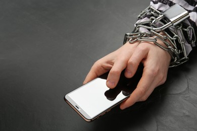 Photo of Prisoner holding smartphone in chained hands at black table, closeup. Internet addiction
