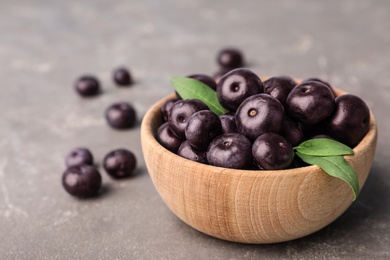 Photo of Bowl of fresh acai berries on grey stone table, closeup view. Space for text