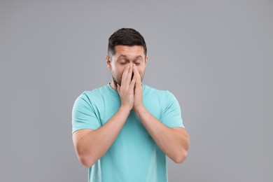 Allergy symptom. Man sneezing on light grey background