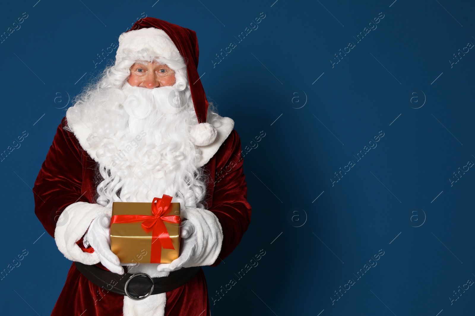 Photo of Authentic Santa Claus with gift box on blue background. Space for text