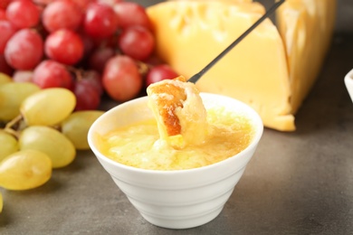 Photo of Piece of bread over bowl with delicious cheese fondue on gray table