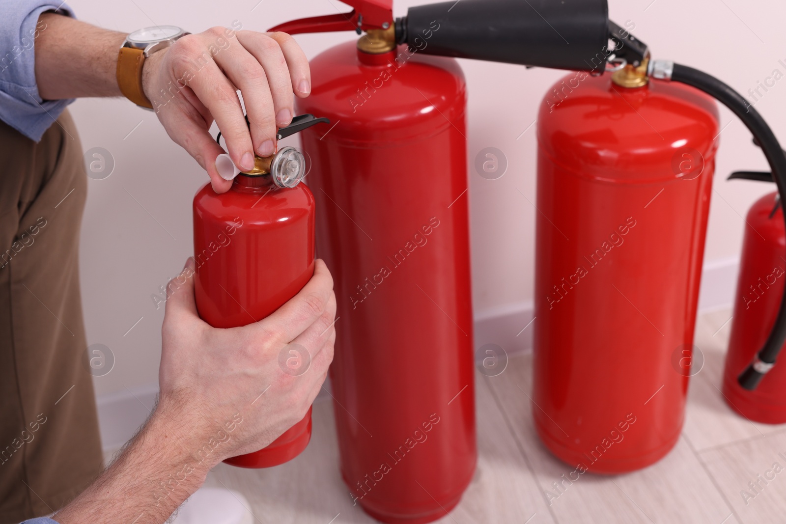 Photo of Man checking quality of fire extinguishers indoors, closeup