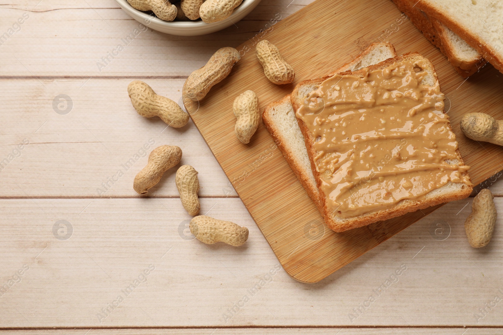 Photo of Delicious toasts with peanut butter and nuts on light wooden table, flat lay. Space for text