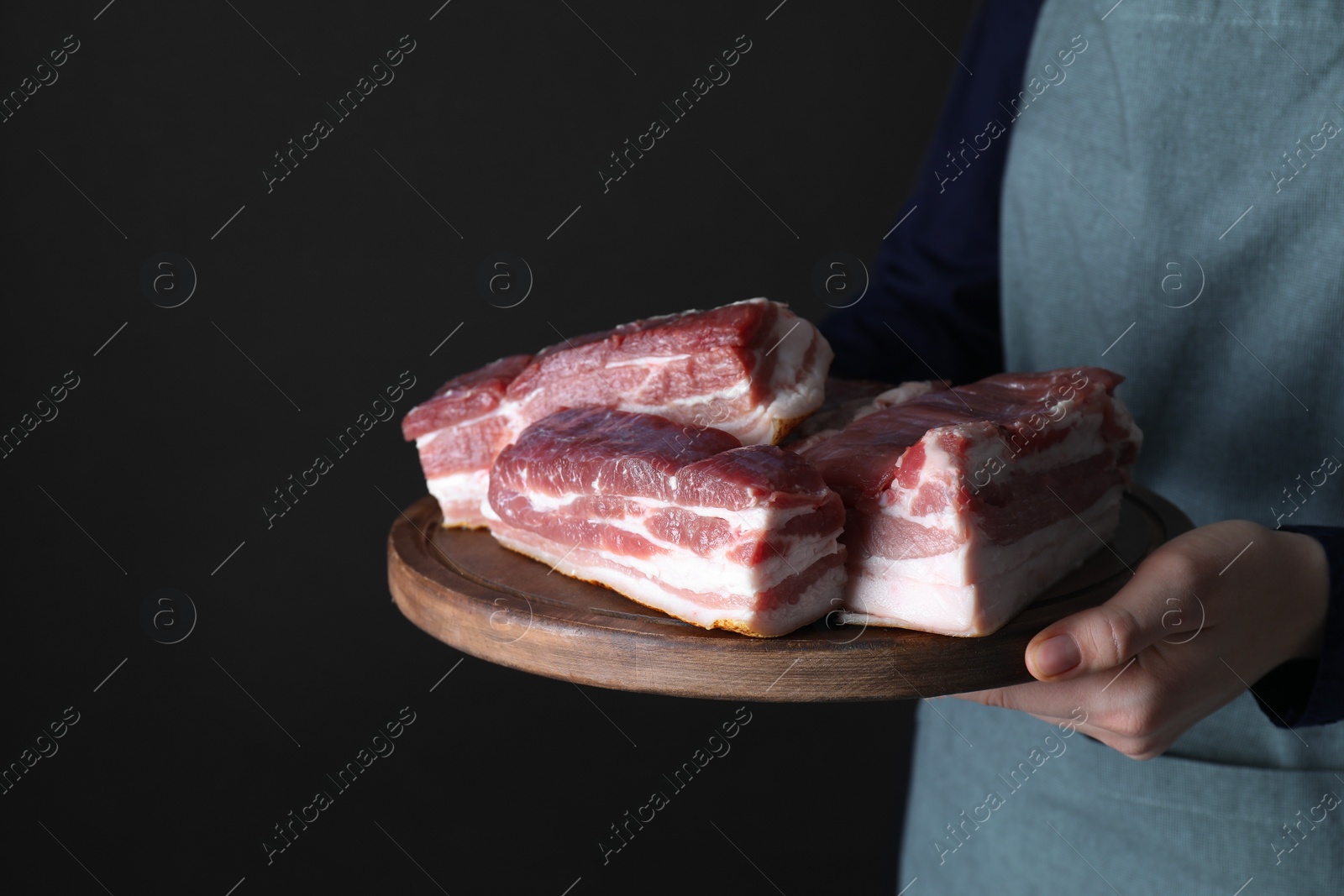 Photo of Woman holding wooden board with pieces of raw pork belly on black background, closeup. Space for text