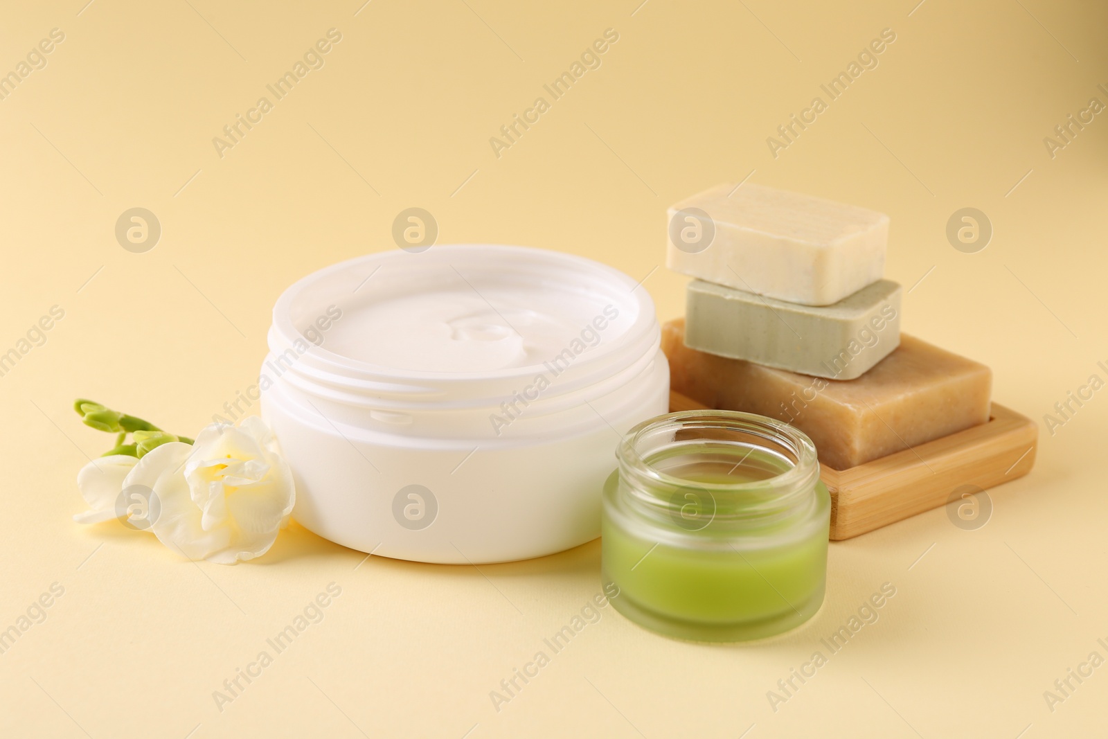 Photo of Moisturizing cream in open jars, soap bars and freesia flower on beige background. Body care products