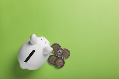 Photo of Ceramic piggy bank and coins on light green background, top view with space for text. Financial savings