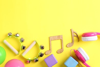 Photo of Baby song concept. Wooden notes, tambourines and toys on yellow background, flat lay. Space for text