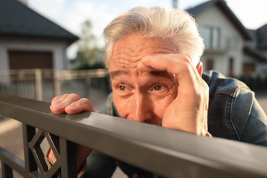 Photo of Concept of private life. Curious senior man spying on neighbours over fence outdoors, closeup