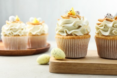 Photo of Tasty Easter cupcakes with vanilla cream and candies on gray table, selective focus