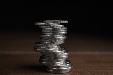 Many coins stacked on wooden table against black background