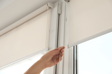 Photo of Woman opening modern roll blinds on window in room, closeup