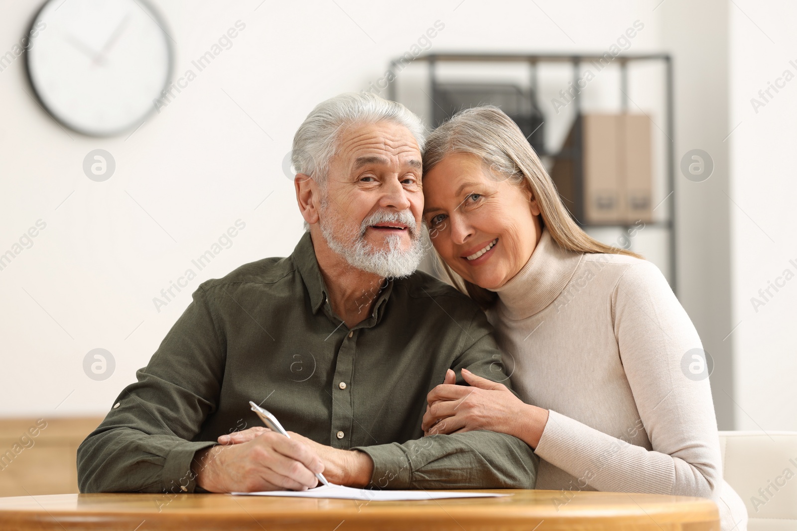 Photo of Happy senior couple signing Last Will and Testament indoors