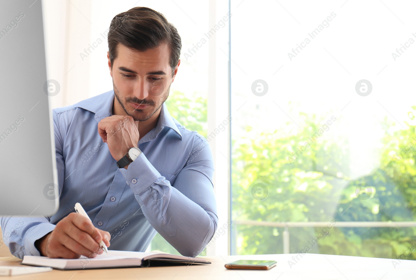 Photo of Handsome young man working with notebook at table in office