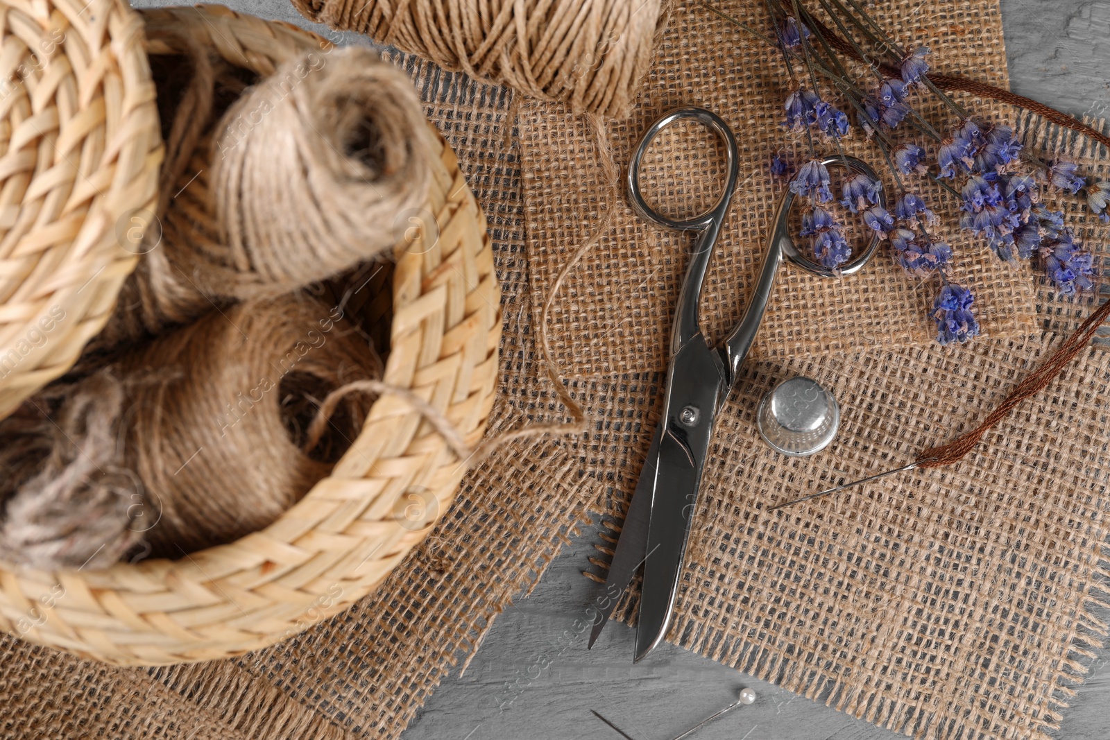 Photo of Pieces of burlap fabric and sewing tools on grey wooden table, flat lay