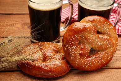 Photo of Tasty freshly baked pretzels, spikelets and mugs of beer on wooden table, closeup