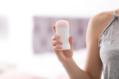 Photo of Beautiful young woman holding deodorant in bedroom, closeup. Space for text