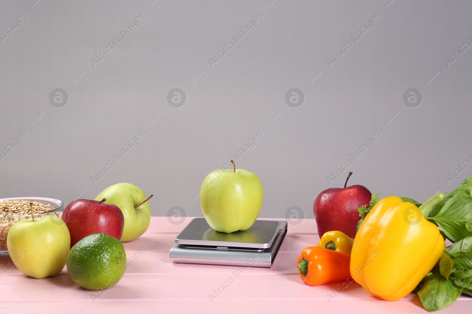 Photo of Kitchen scale with apple and vegetables on pink wooden table, space for text