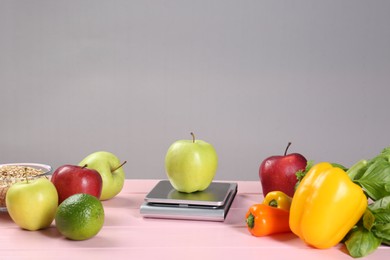 Photo of Kitchen scale with apple and vegetables on pink wooden table, space for text