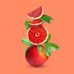 Stacked cut and whole red oranges with green leaves on coral color background