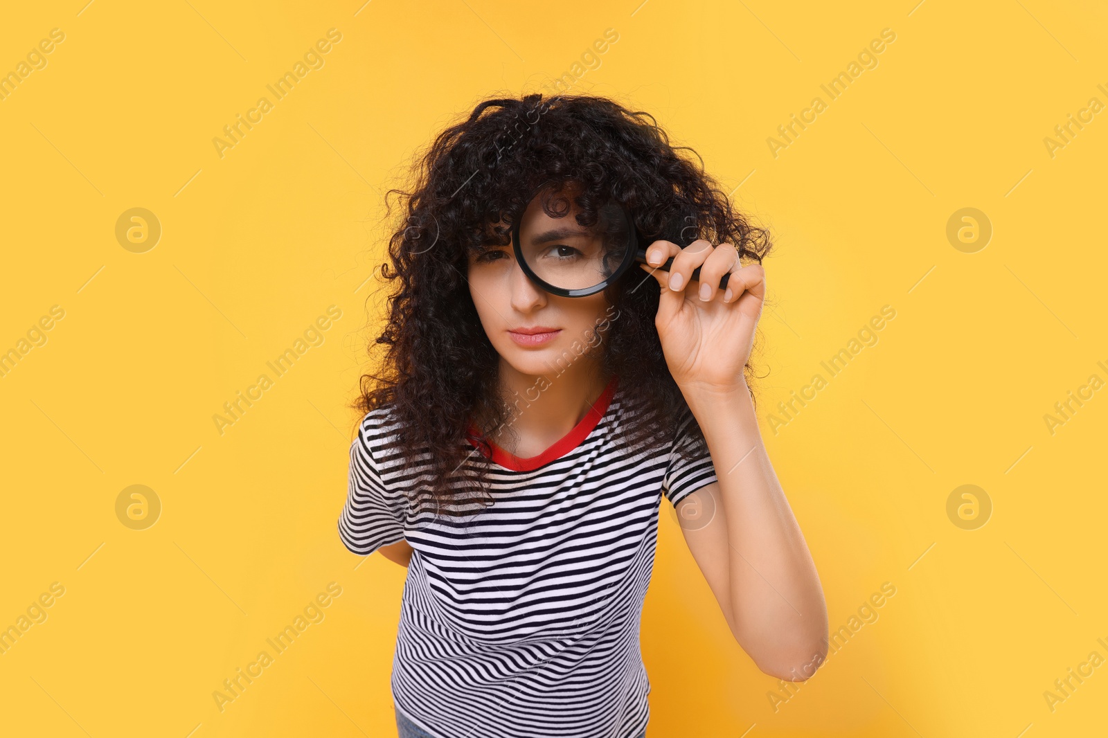 Photo of Curious young woman looking through magnifier glass on yellow background
