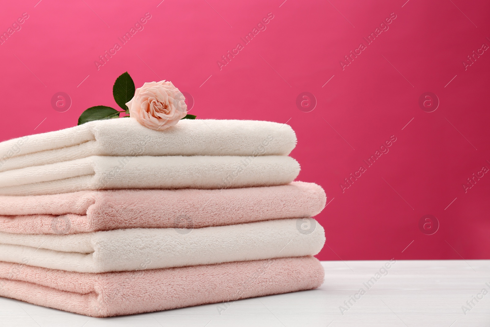 Photo of Stack of soft clean towels with beautiful flower on table against color background. Space for text