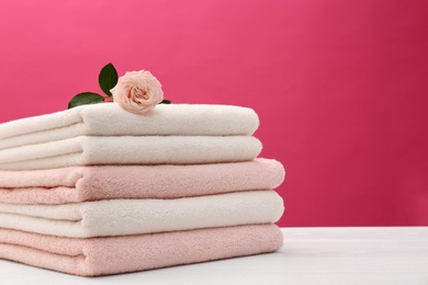 Stack of soft clean towels with beautiful flower on table against color background. Space for text