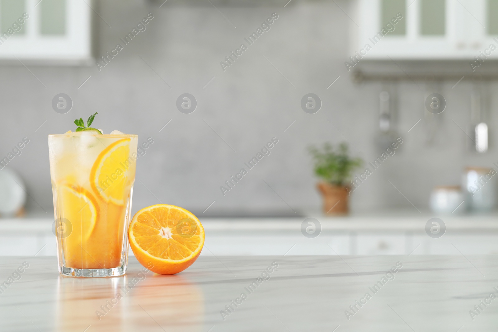 Photo of Tasty refreshing drink with orange on white marble table in kitchen. Space for text