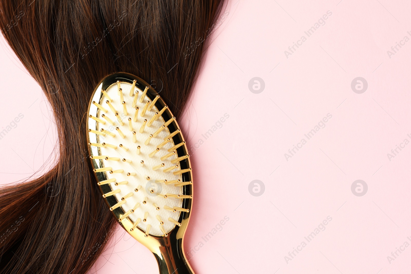 Photo of Stylish brush with brown hair strand on pink background, top view. Space for text