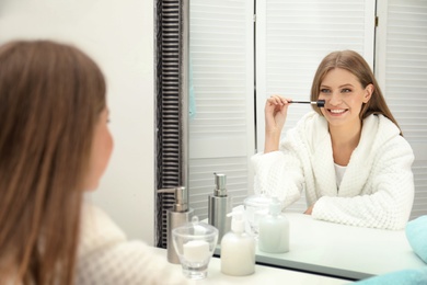 Young woman with long eyelashes and brush near mirror in bathroom