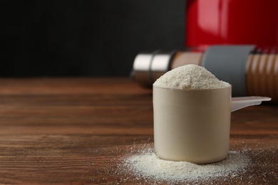 Photo of Measuring scoop of protein powder on wooden table. Space for text