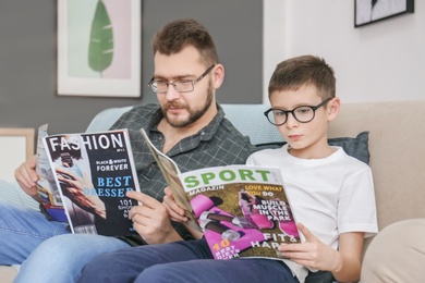 Photo of Little boy and his dad reading magazines at home