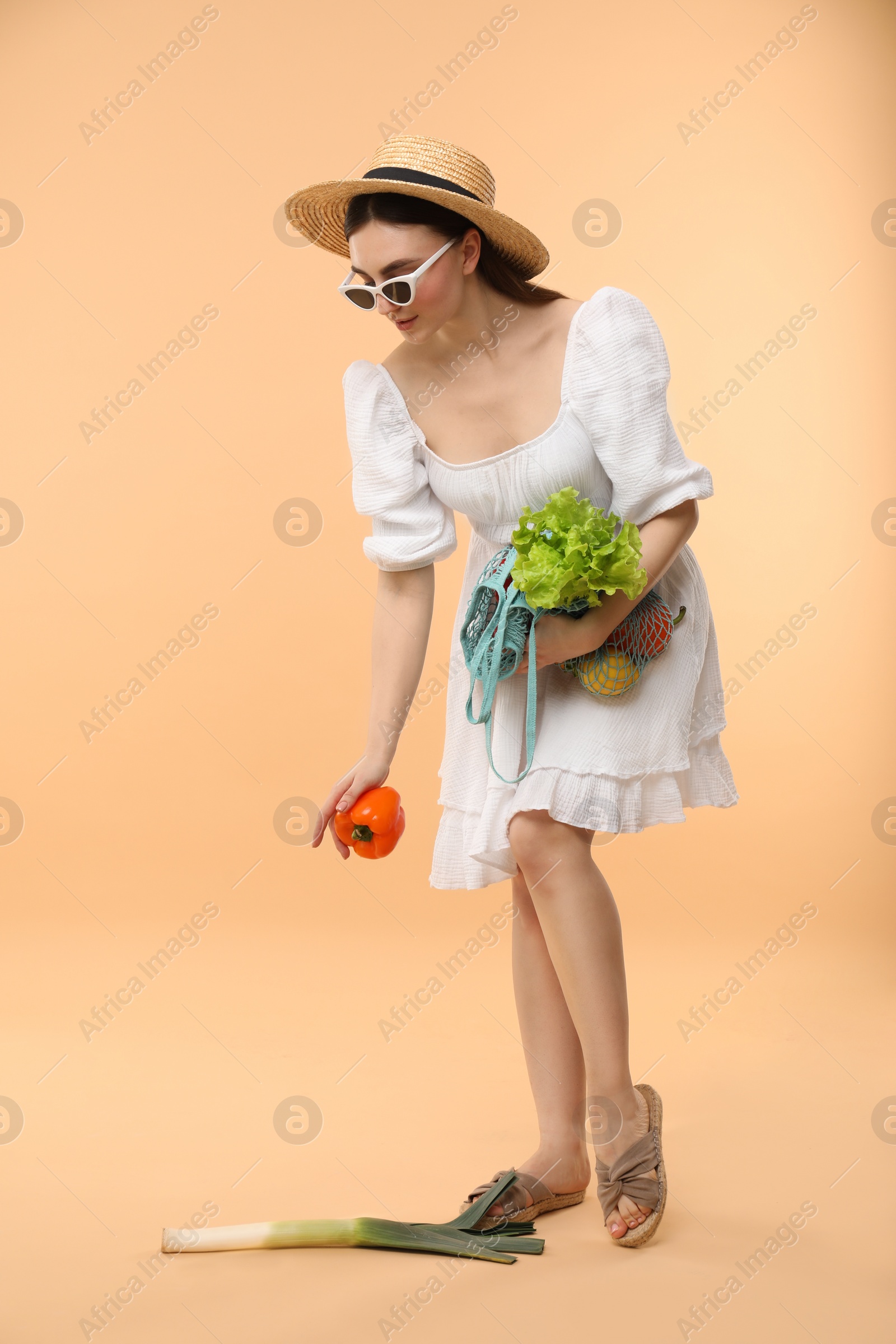 Photo of Woman with string bag of fresh vegetables on beige background