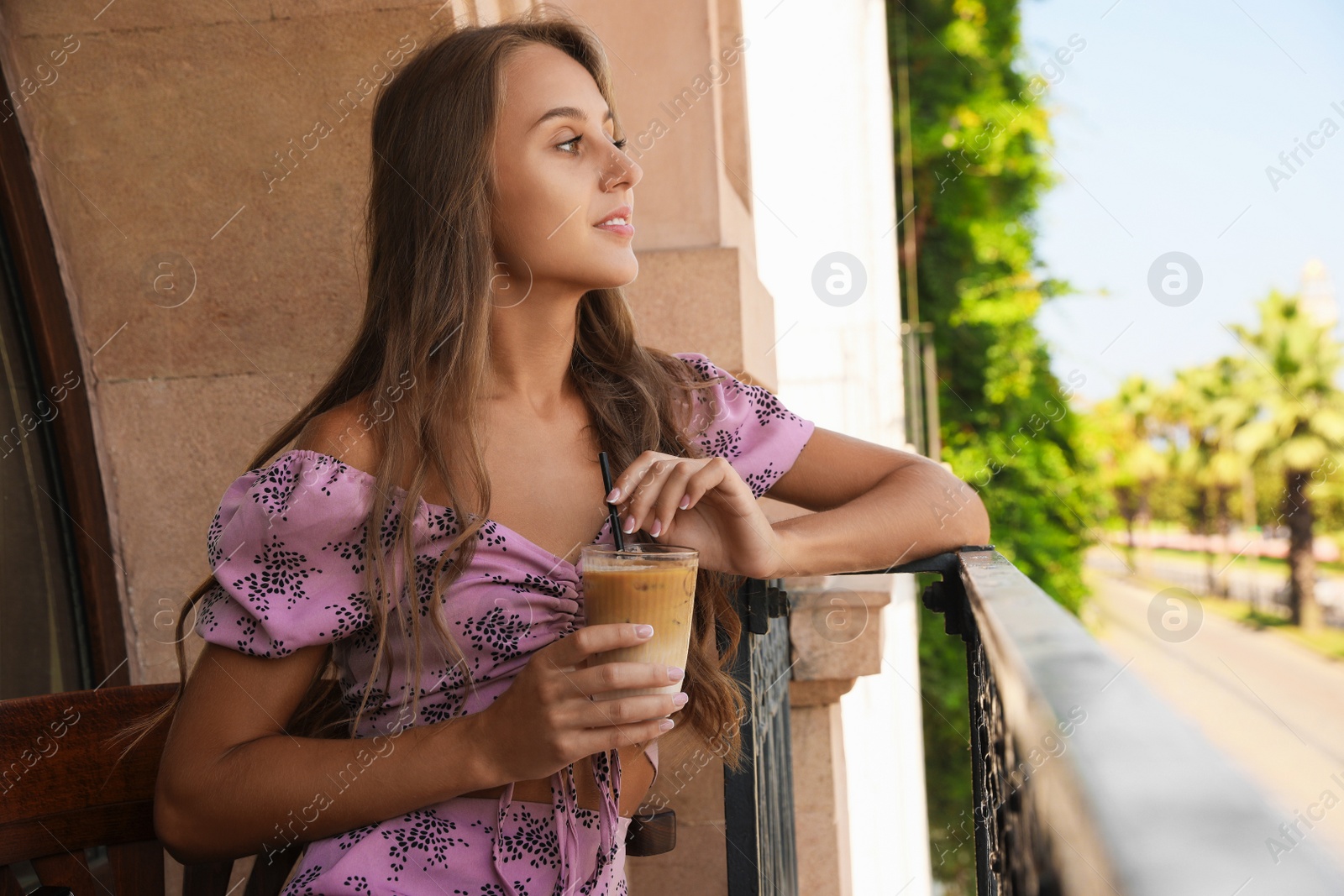 Photo of Young woman with glass of coffee sitting on balcony