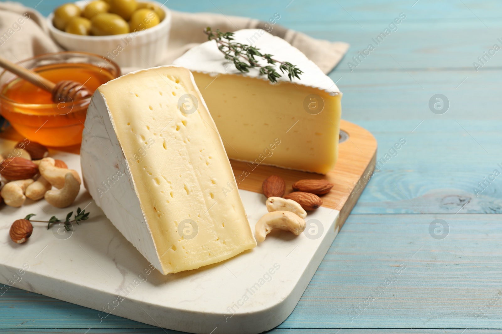 Photo of Tasty Camembert cheese with thyme, honey and nuts on light blue wooden table. Space for text