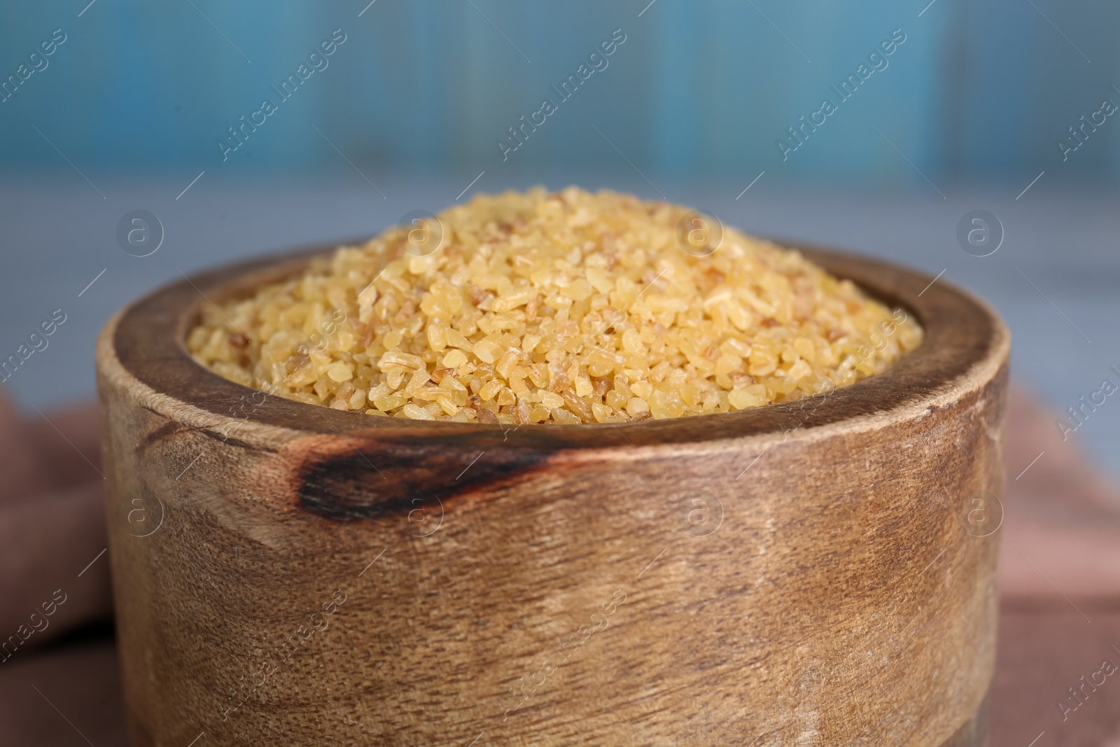 Photo of Wooden bowl with uncooked bulgur on table, closeup