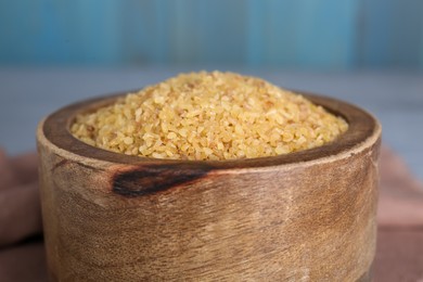 Photo of Wooden bowl with uncooked bulgur on table, closeup