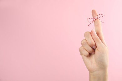 Photo of Woman showing index finger with tied bow as reminder on pink background, closeup. Space for text