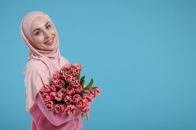 Happy woman in hijab with beautiful bouquet on light blue background. Space for text