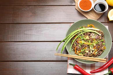 Photo of Stir-fry. Delicious cooked noodles with chicken and vegetables in bowl on wooden table, flat lay. Space for text