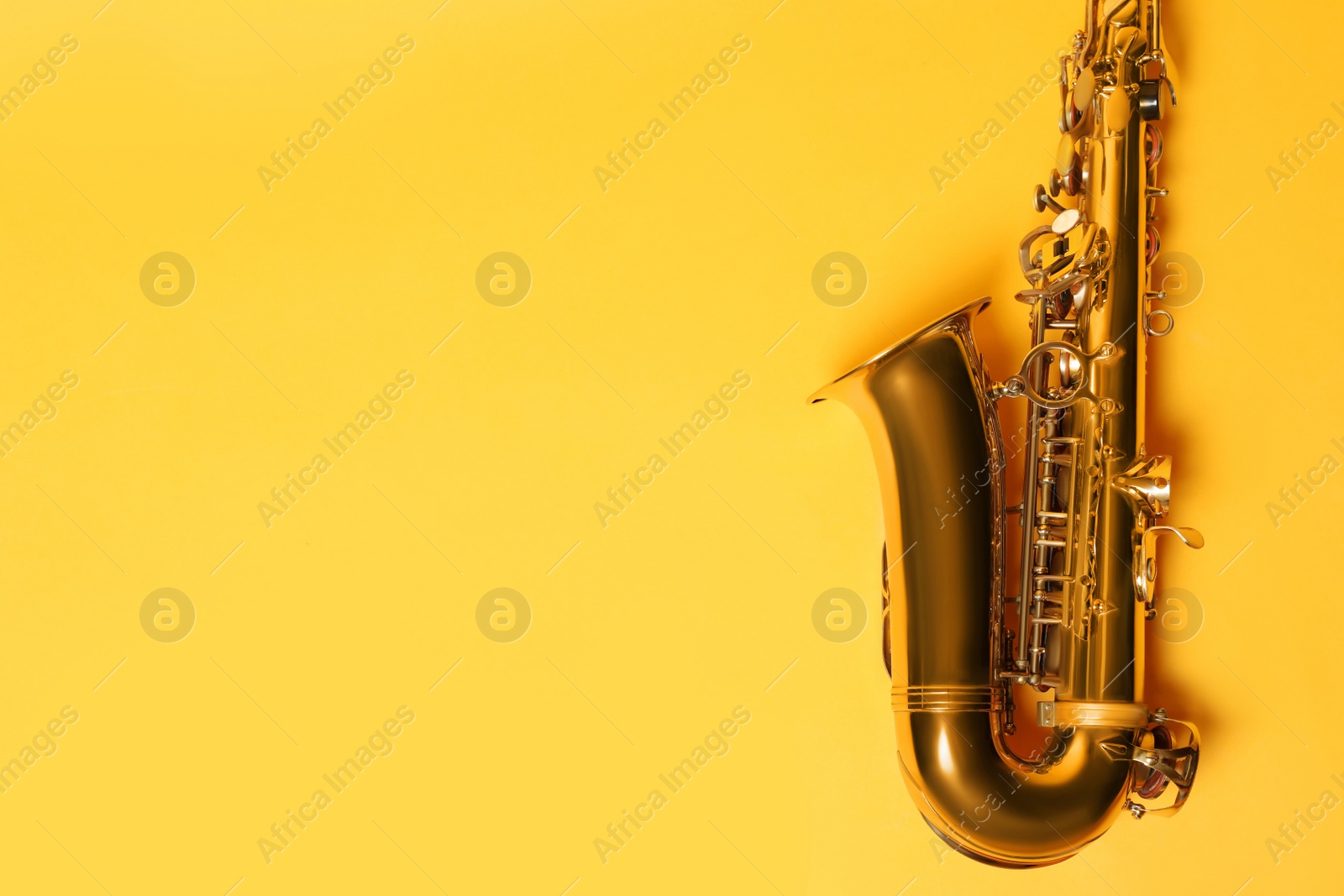 Photo of Beautiful saxophone on yellow background, top view. Space for text