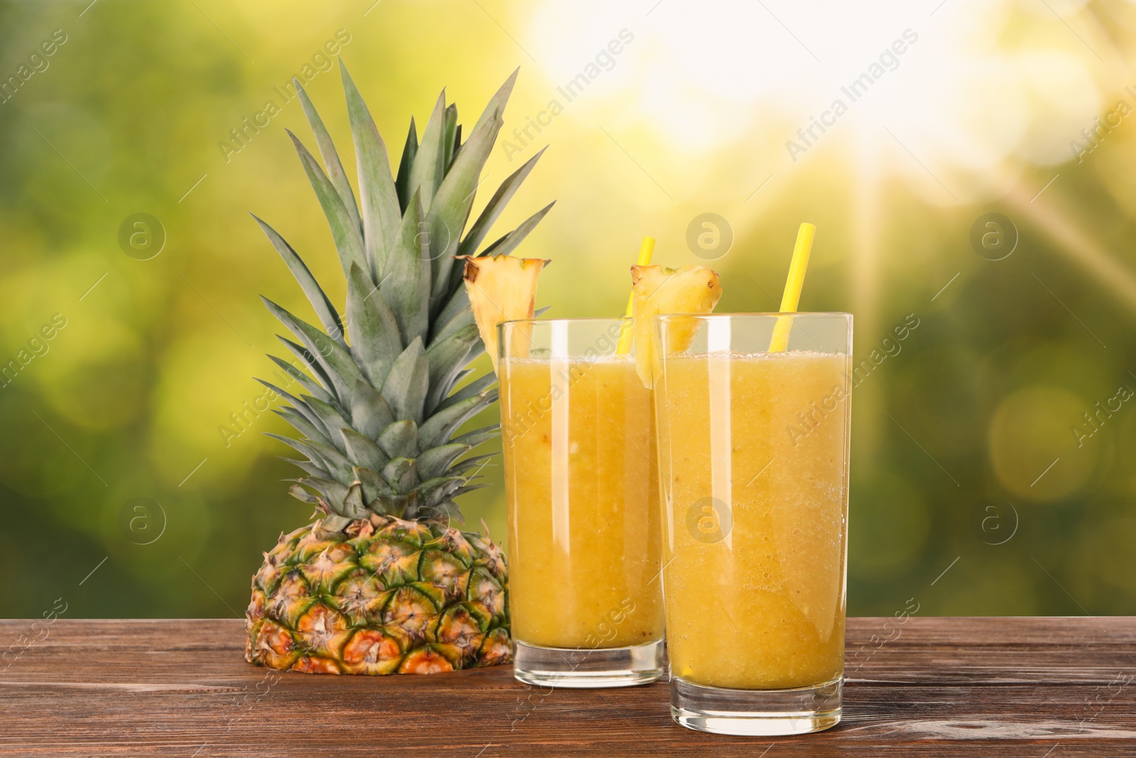 Image of Tasty pineapple smoothie in glasses on wooden table against blurred background