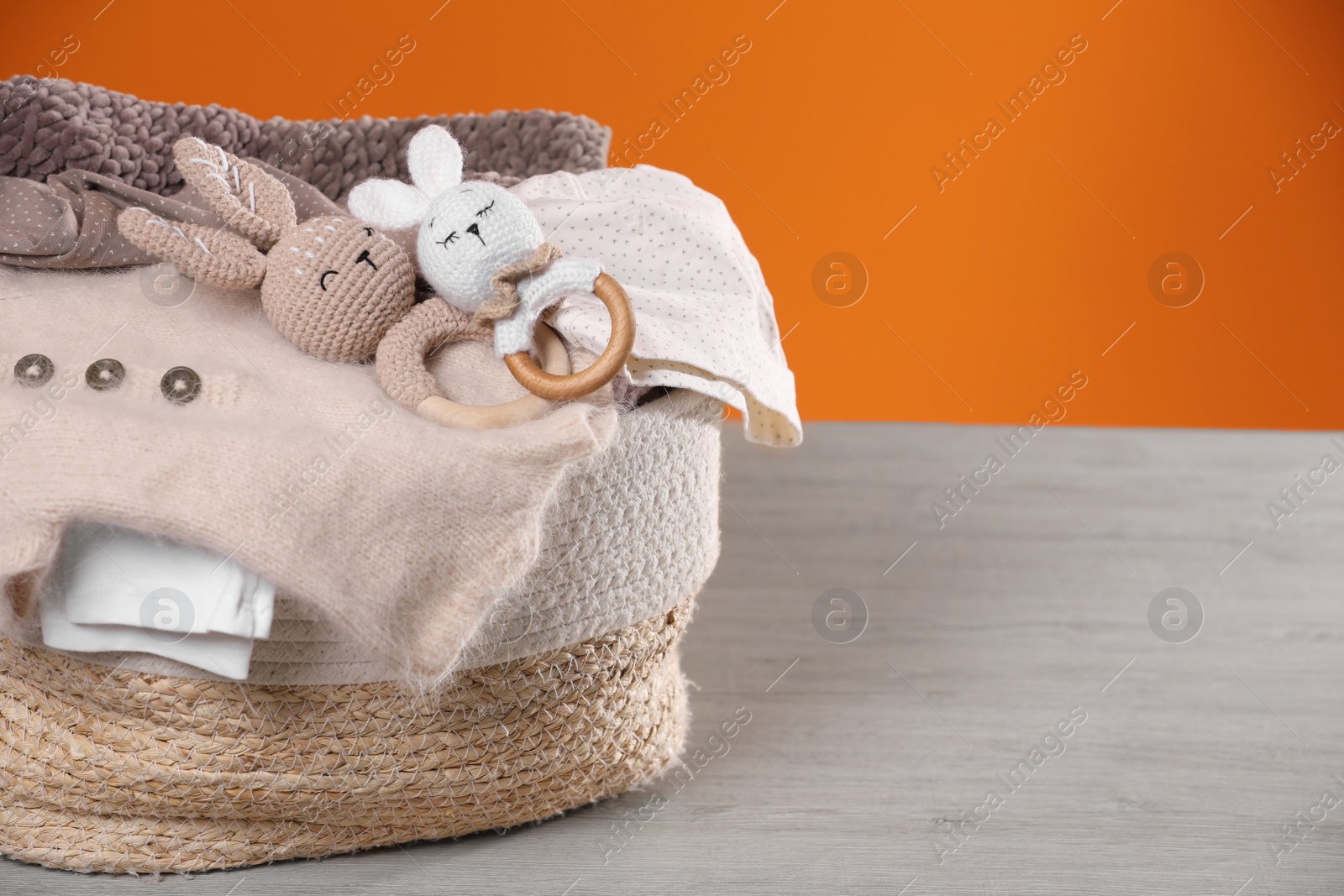 Photo of Laundry basket with baby clothes and crochet toys on wooden table against orange background, space for text