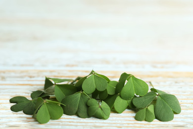 Pile of clover leaves on light wooden table, space for text. St. Patrick's Day symbol