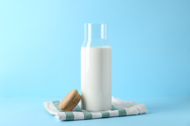 Photo of Glass carafe of fresh milk and lid on light blue background