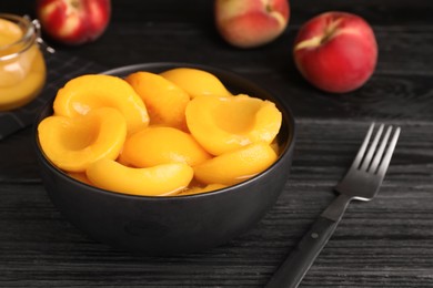 Canned peach halves and fork on black wooden table