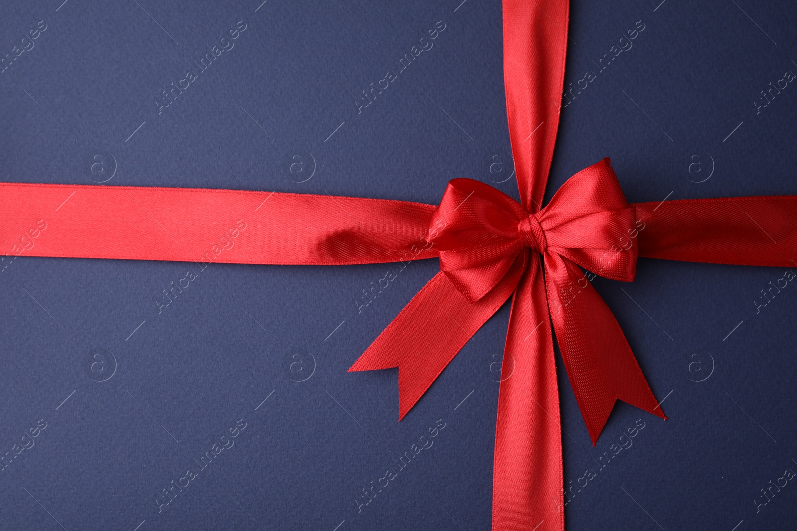 Photo of Red satin ribbon with bow on blue background, top view