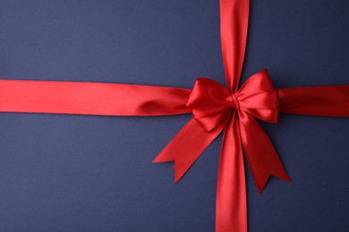 Photo of Red satin ribbon with bow on blue background, top view