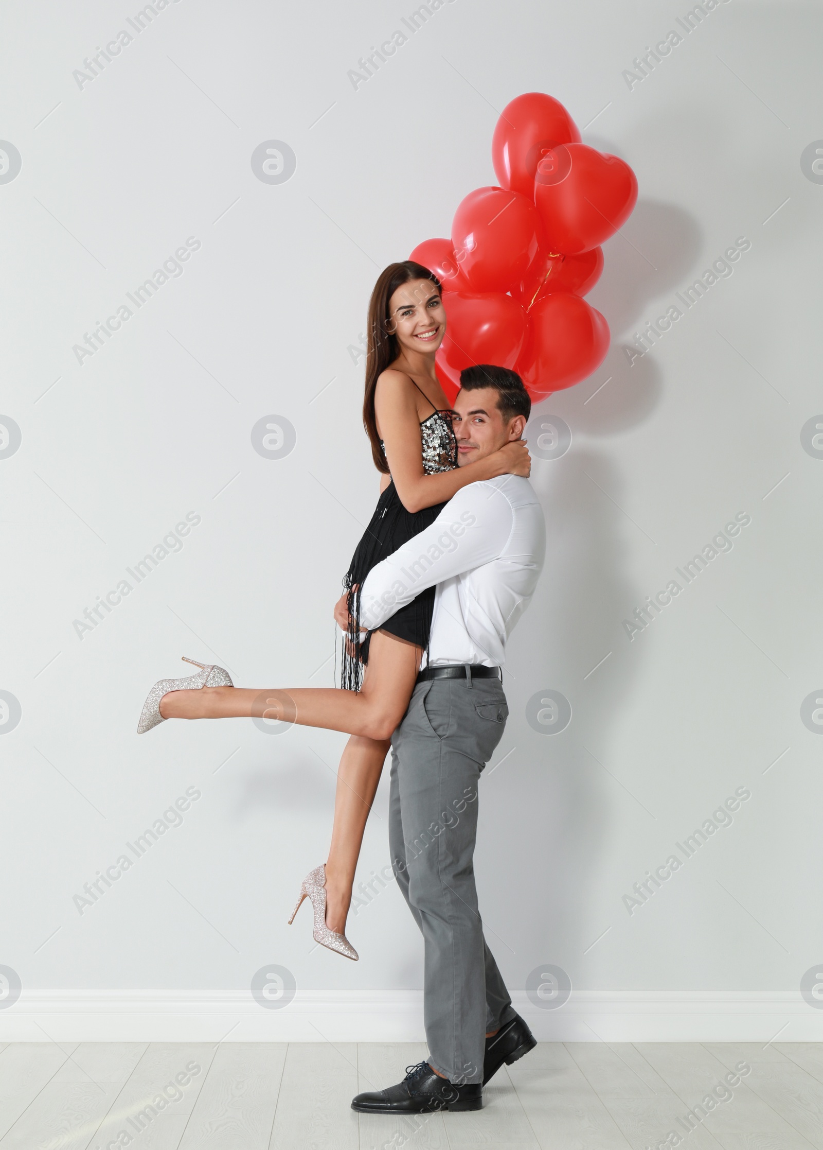 Photo of Beautiful couple with heart shaped balloons near light wall