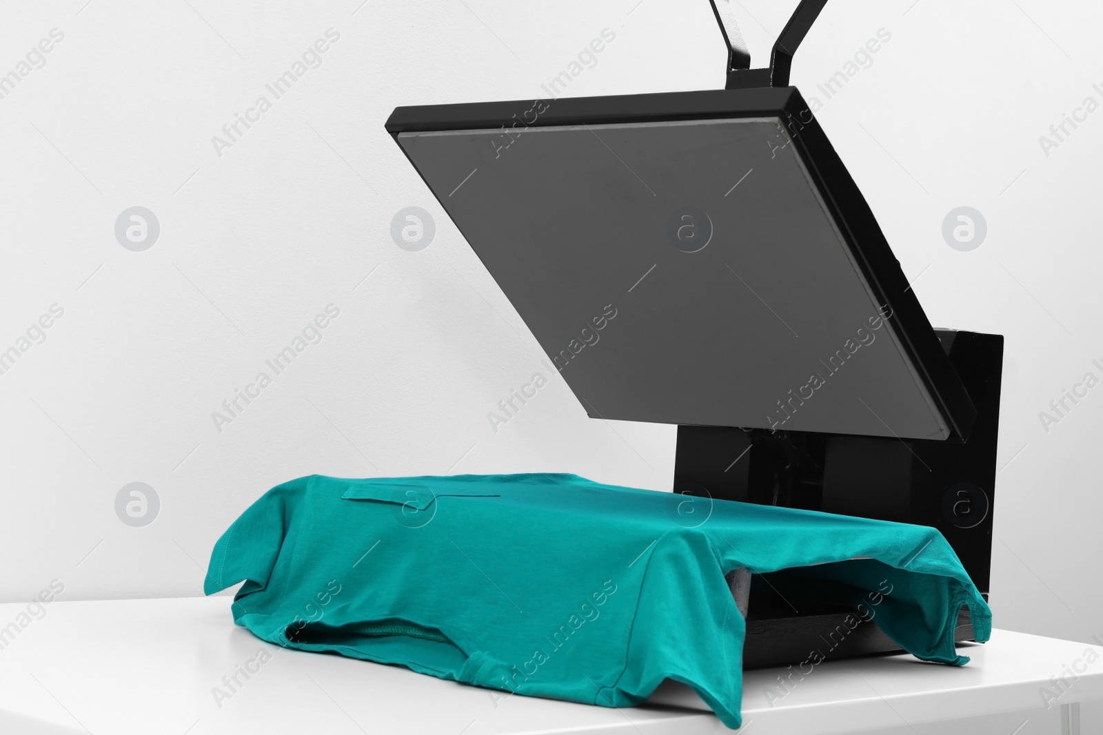 Photo of Heat press machine with t-shirt on table against light background