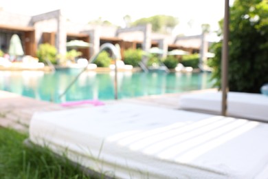 Sun loungers near outdoor swimming pool, blurred view. Luxury resort